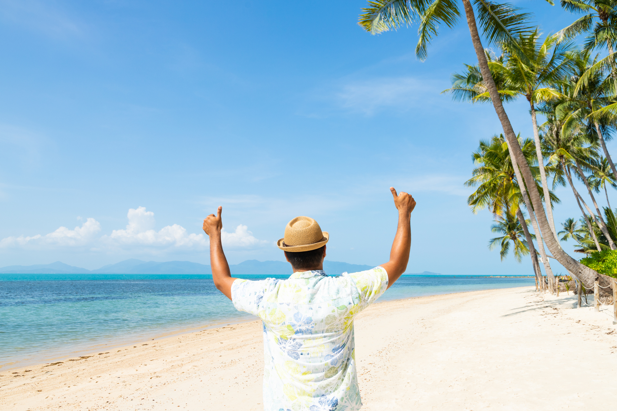 Rear View Of Man With Arms Outstretched Gesturing While Standing At Beach Against Sky Rear View of a man walking on a tropical beach with two thumbs up.