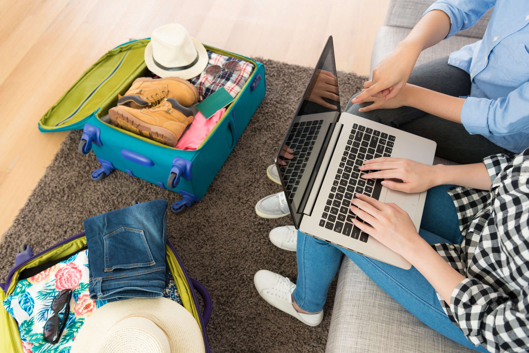 high angle view photo of two people using computer High angle view photo of two people using computer laptop planning travel experiences and pointing screen when they packing luggage at home.