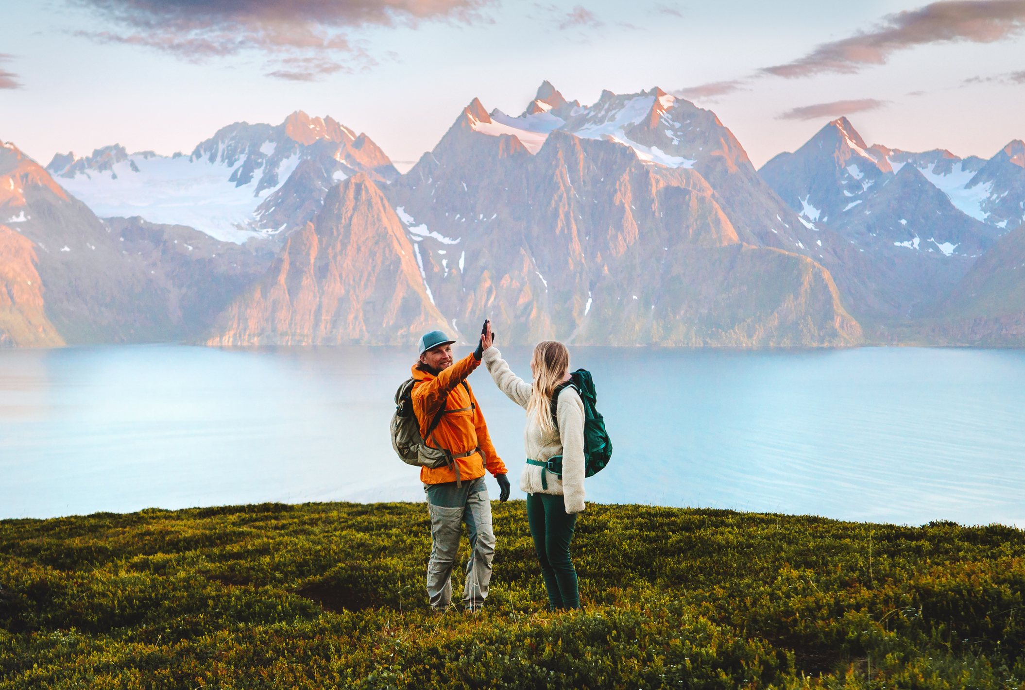 Man and woman backpackers high-fiving on a mountain summit in Norway, celebrating teamwork and friendship during an outdoor hiking adventure, representing active travel, sustainable tourism, and adventure lifestyle.